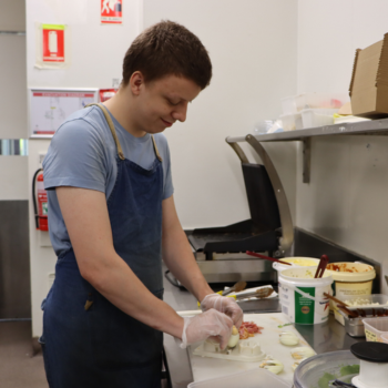 Person wearing an apron and gloves preparing food in a commercial kitchen.